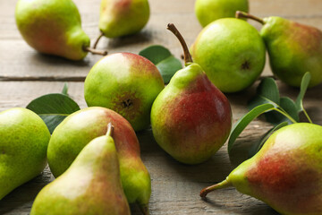 Fresh ripe pears and green leaves on wooden table, closeup