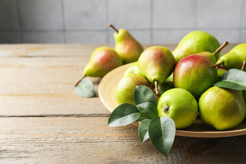 Fresh ripe pears and green leaves on wooden table, closeup. Space for text