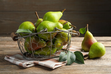 Fresh ripe pears in metal basket and green leaves on wooden table