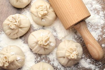 Uncooked khinkalis (dumplings) with rolling pin and flour on wooden table, flat lay