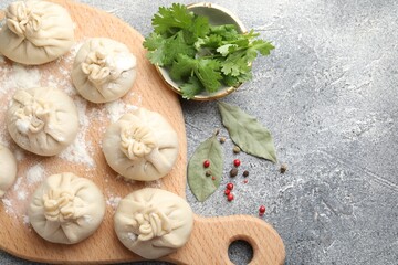 Uncooked khinkalis (dumplings) with peppercorns, flour, parsley and bay leaves on grey table, flat lay. Space for text