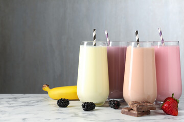 Tasty milkshakes in glasses and ingredients on white marble table, space for text