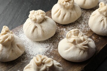 Uncooked khinkalis (dumplings) with flour on black table, closeup