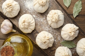 Uncooked khinkalis (dumplings) with flour, oil and bay leaves on wooden table, flat lay