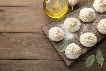 Uncooked khinkalis (dumplings) with flour, garlic and bay leaves on wooden table, flat lay. Space for text