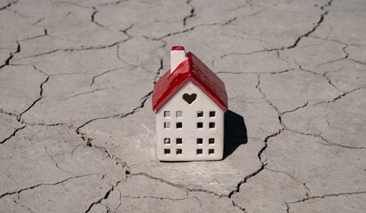 A ceramic house  against the background of clay cracked by the heat in the desert