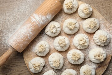 Fototapeta premium Uncooked khinkalis (dumplings) and rolling pin on wooden table, top view