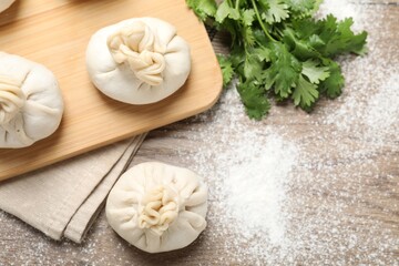 Uncooked khinkalis (dumplings) and cilantro on wooden table, flat lay. Space for text