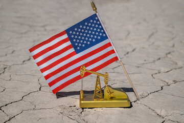 A miniature gold oil pump and US flag on cracked clay in the desert