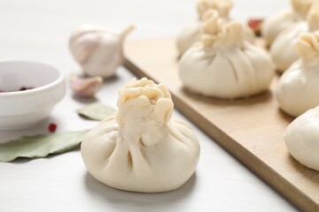 Uncooked khinkalis (dumplings) and spices on white wooden table, closeup