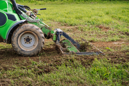 Land work by the territory improvement. Small tractor with a ground leveler for moving soil, turf. A green mini skid steer loader clear the construction site. Machine for agriculture work. Copy space.