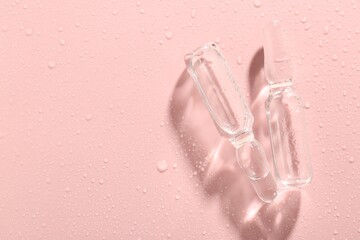 Glass ampoules with liquid and water drops on pink background, flat lay. Space for text