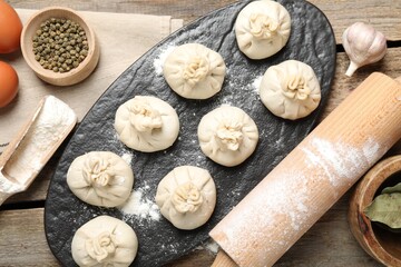 Fototapeta premium Uncooked khinkalis (dumplings), flour, spices, eggs and rolling pin on wooden table, flat lay