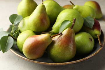 Fresh ripe pears and green leaves on light grey table, closeup