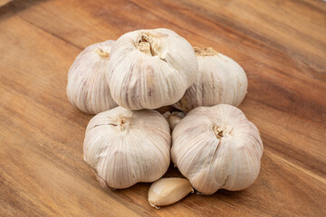 A cluster of fresh garlic bulbs rests on a wooden cutting board in a kitchen. The bulbs showcase...