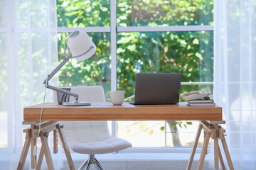 Home workspace. Laptop and stationery on wooden desk near window indoors