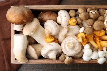 Different raw mushrooms in crate on wooden table, top view