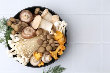 Different raw mushrooms in bowl and dill on white tiled table, flat lay. Space for text