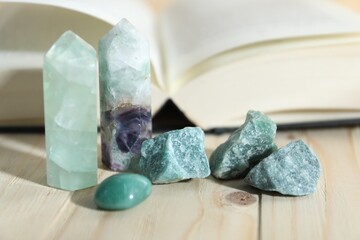 Different healing stones and book on wooden table, closeup
