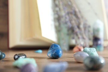 Different healing stones and book on wooden table, closeup
