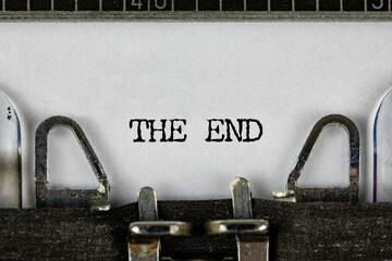 Closeup of a blue retro typewriter and the text the end written with it in a yellowish foil. Close...