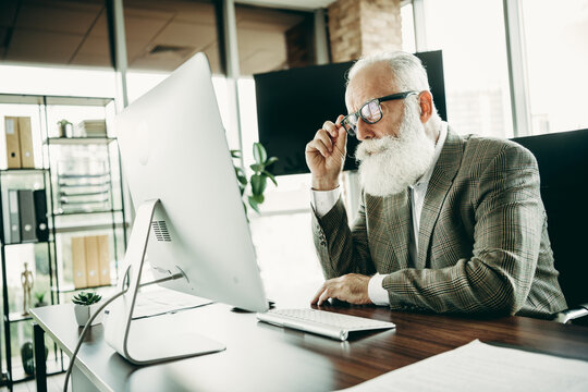 Mature businessman analyzing computer data in a modern office wearing elegant business attire and stylish glasses