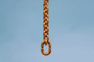 Fototapeta premium A vertical gold chain is suspended against a soft light gray-blue background, showcasing its intricate design and brilliant shine