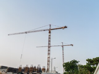 Fototapeta premium Tower crane or mobile crane erected beside under construction building. Yellow color Building crane or Fixed crane used for lifting heavy items or materials from ground to top level for high building