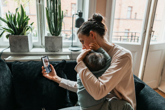 Mother embracing sick son while taking online consultation from pediatrician through smart phone at home