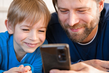 Father and son little boy laughing and using phone. They watching funny videos together, playing...