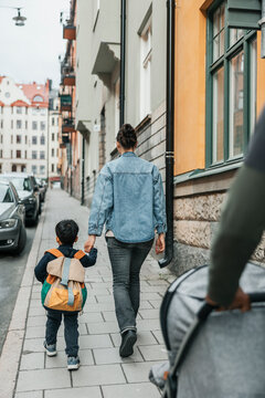Rear view of mother holding hands of son while walking on sidewalk