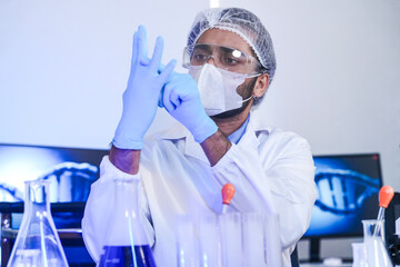 A focused male scientist in full protective gear analyzes a chemical solution in a flask. A dedicated researcher works in a modern laboratory on a medical or pharmaceutical discovery.
