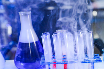 A chemical reaction in a science laboratory. Vapor billows from a flask of purple liquid and a rack of test tubes, creating a dynamic and mysterious scientific background.