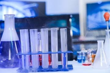 A chemical reaction in a science laboratory. Vapor billows from a flask of purple liquid and a rack...