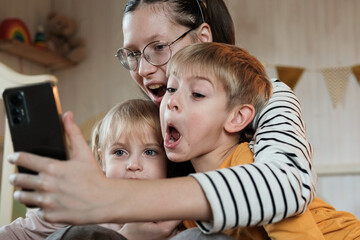 Young Kids Taking a Selfie Photo Together Using Smartphone During Fun Birthday Party in Decorated Room, Copy space. Family Moment. Selfie of Sisters and Brother, Small Children. Happy Childhood