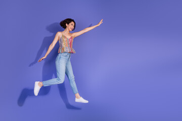 Obraz premium Funky stylish woman in casual fashion jumping joyfully against a purple background in a shiny sequined top and jeans