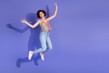 Obraz premium Cheerful female in casual denim and sequined top joyfully jumping against a purple background emphasizing vibrant energy
