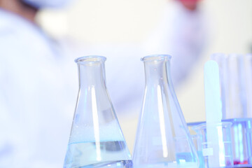 A scientist in protective gear conducts genetic research in a modern lab. He analyzes a chemical in a flask with a DNA helix displayed on a monitor in the background.