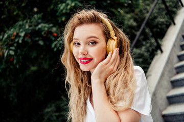 Smiling young woman outdoors enjoying music wearing headphones, showcasing happiness and trendy...