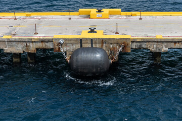 Image of one large black netless foam-filled marine fender chained to cruise ship dock.