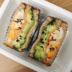 A colorful sandwich made with layers of vegetables, eggs, and seeds, presented in a takeout...