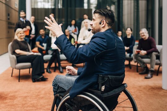 Physically disabled male delegate wearing headset giving lecture at business summit in congress center