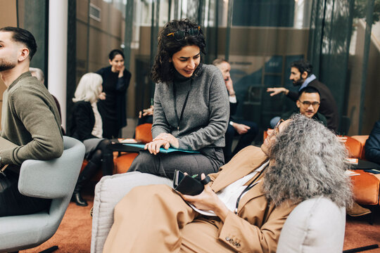 Businesswoman talking with mature female colleague sitting on armchair at networking event in congress center