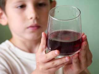 Child holding a glass with juice - A close-up portrait of a young boy with a serious and...
