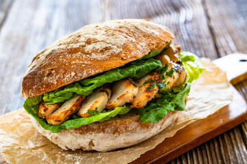 Takeaway sandwich with slices of grilled chicken breast on wooden table	