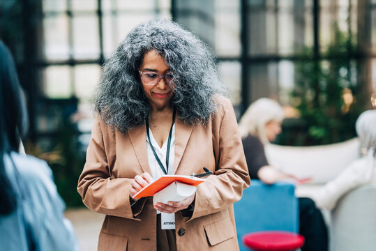 Gray haired mature female business expert reading book about seminar instructions at convention center