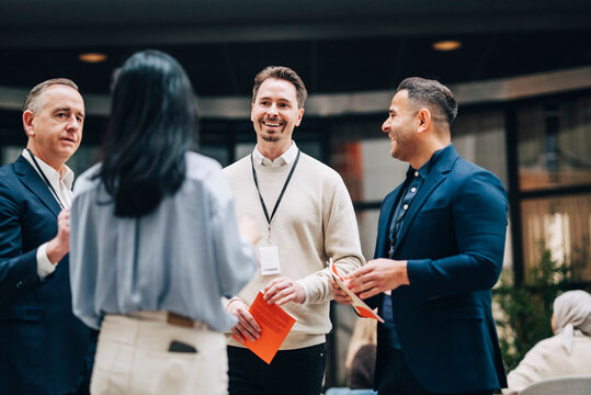 Smiling male business professionals talking with female colleague at networking event in convention center