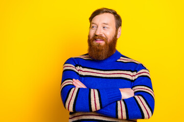 Trendy young man with a red beard standing confidently against a bright yellow background in a striped pullover