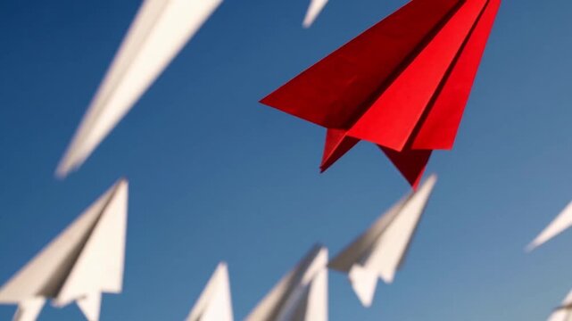 Concepts of transformation and divergence illustrated by solitary crimson origami aircraft veering away from flock of white ones, representing leadership, originality, novel thought, alteration, fash