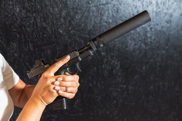 Close-up of a woman's hands with a manicure holding a modern handgun equipped with a silencer and...
